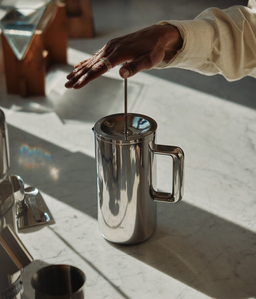 Hand pressing Aarke stainless steel French Press plunger on marble countertop.