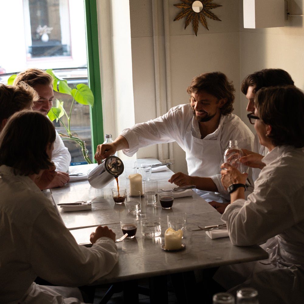 People in a dining setting with one person pouring a coffee from the Aarke Coffee Press.