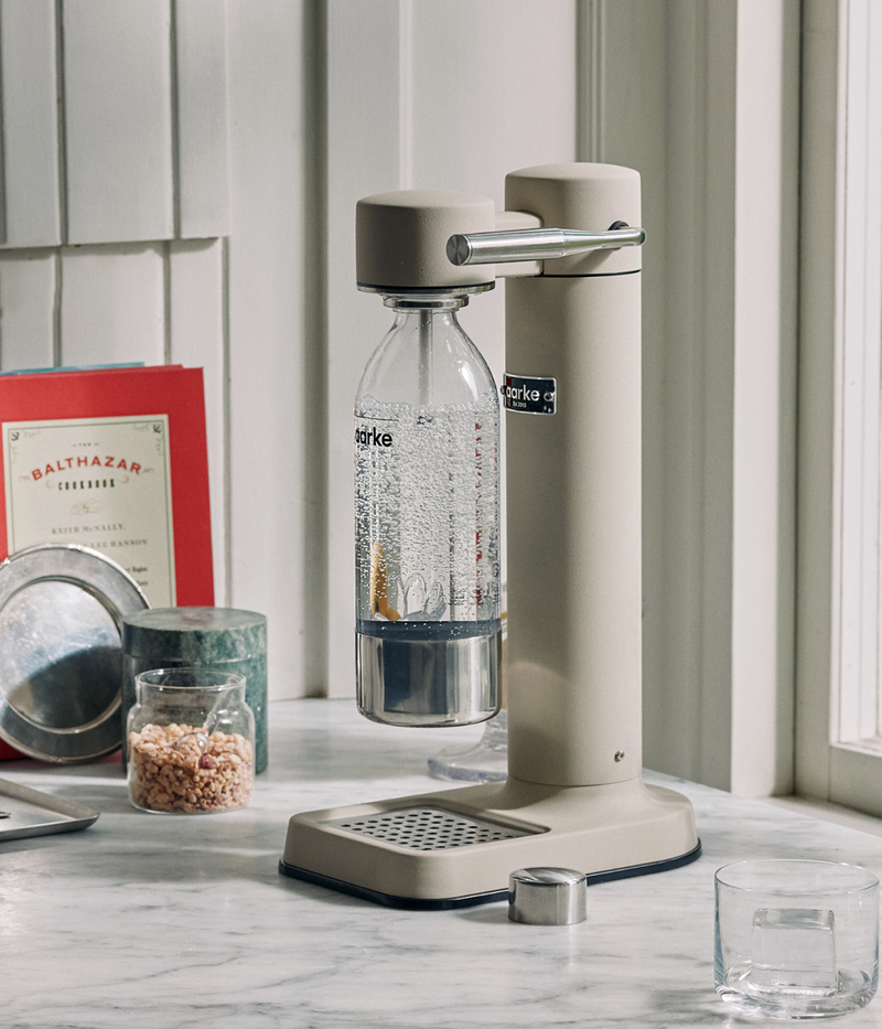 Aarke Carbonator 3 in sand finish on a marble countertop, carbonating water in an Aarke PET bottle.