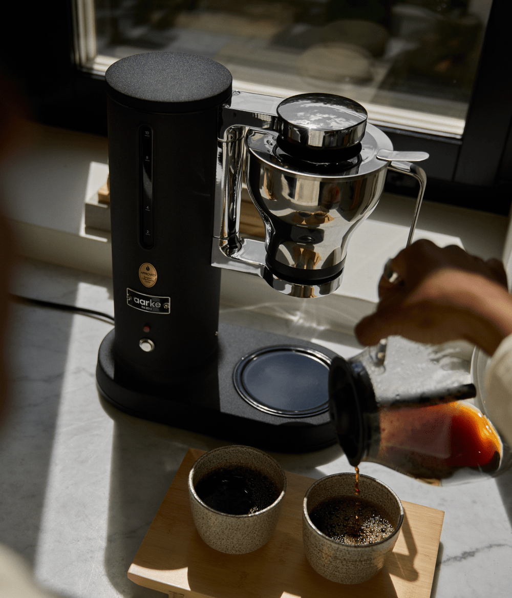 Person pouring coffee from the Aarke coffee maker Matte Black into two cups on a marble surface.